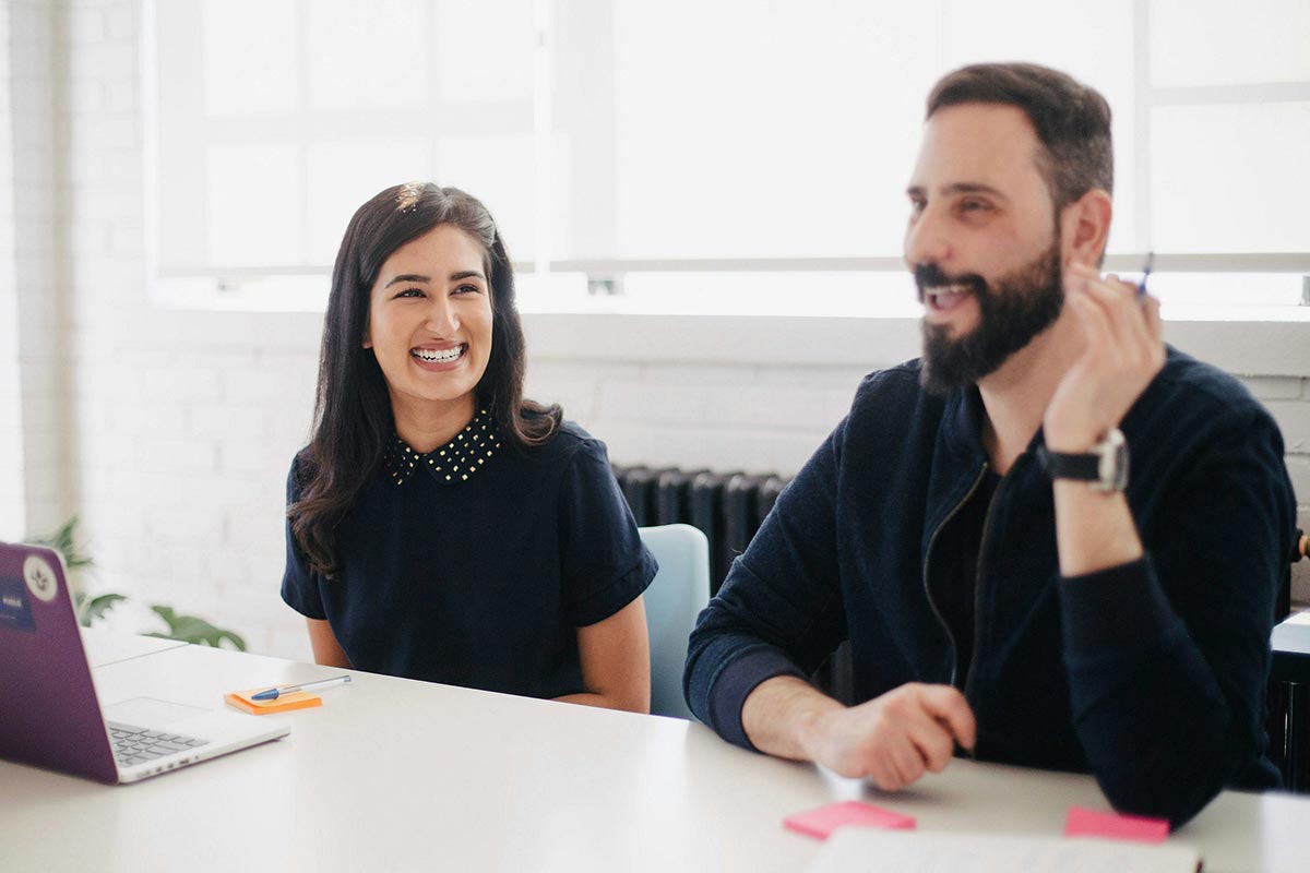 Two coworkers smiling and talking during a meeting in a bright boardroom