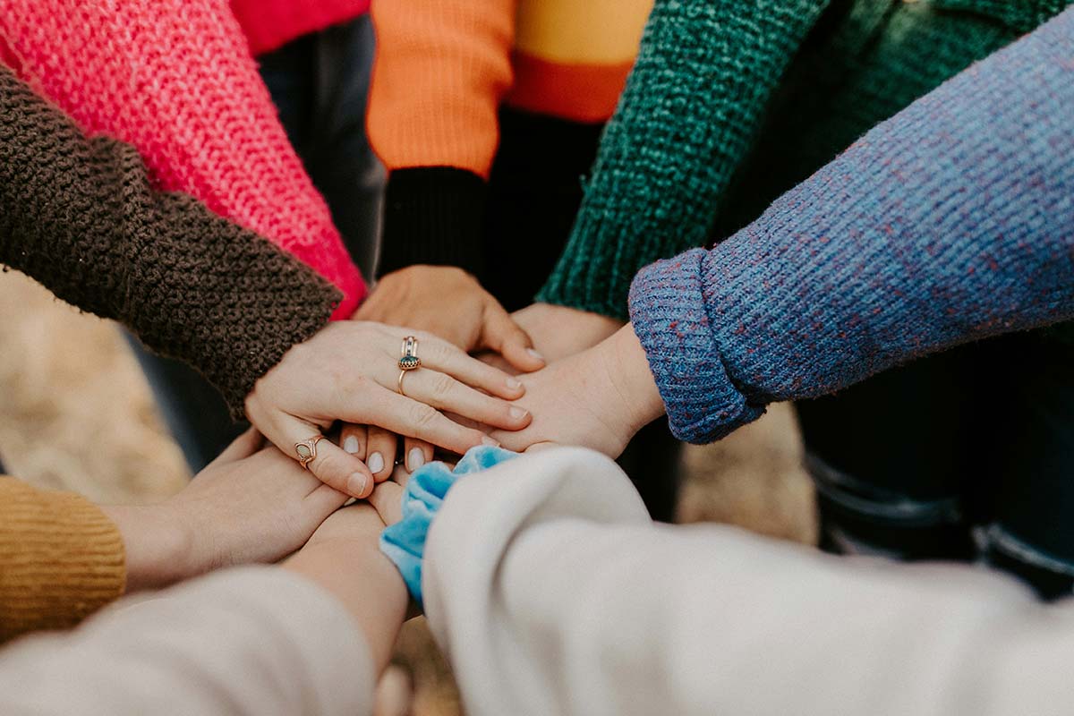 Colleagues sitting in a circle placing their hands together in a team huddle